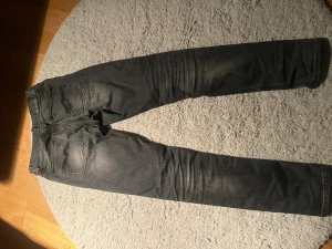 Svarta slim fit jeans från Nudie Jeans - Snygga svarta jeans från Nudie Jeans i modellen slim fit med klassisk femficksdesign och subtila slitningar. Jeansen har en smal passform och är tillverkade i mjukt jeansmaterial. Perfekt för dig som gillar en stilren och modern look.