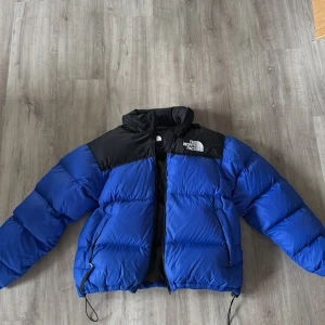 Blå och svart pufferjacka North Face - The North Face jacka med broderad logga på bröstet och ryggen. Jackan har huva, helt ny dragkedja. Om de är minus 25 grader svettas man i denna jacka. Köptes ny för 7000kr då denna var den dyraste modellen för något är sedan! Storlek L men passar Allt. Bvsa