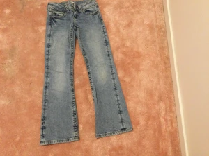 Bootcut jeans från Gina Tricot ljusblå - Snygga ljusblå bootcut jeans från Gina Tricot i klassisk femficksmodell. Jeansen har normal passform, dragkedja och knapp framtill samt coola detaljer på bakfickorna. Perfekt för dig som gillar retrovibbar och bekväma jeans.