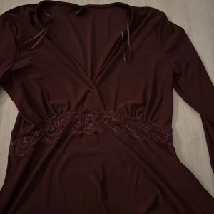 Vinröd omlottklänning från Gina Tricot - Supersnygg vinröd blus från Gina Tricot med lång ärm och spetsdetalj i midjan.