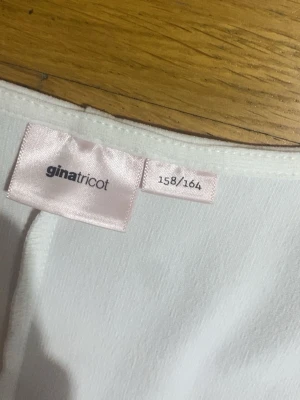Vit blus med fyrkantig ringning Gina Tricot - Säljer en vit blus från Gina Tricot i storlek 158/164. Toppen har lång ärm, markerad midja och en snygg fyrkantig ringning. Tyget är slätt och lätt stretchigt, vilket ger en bekväm passform och en clean look.