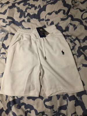 Vita shorts från Polo Ralph Lauren - Säljer ett par fräscha vita shorts från Polo Ralph Lauren med elastisk midja och snörning. Klassisk svart logga broderad på benet och två sidofickor. Perfekta för sommaren och riktigt clean look.