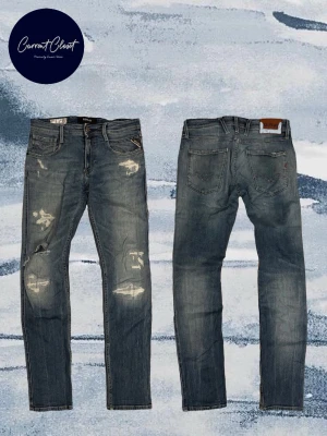 Replay jeans med slitningar, blå, W30/L32 - Säljer ett par Replay jeans i blå tvätt med snygga slitningar och lagade detaljer på benen. Modellen har klassisk femficksdesign, raka ben och är gjorda i ekologisk bomull. Perfekta för dig som gillar en avslappnad och trendig look. Hålet är igenom men går att sy själv eller hos skräddare