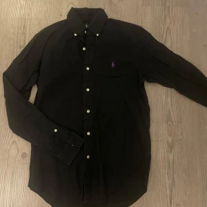 Ralph Lauren skjorta  - skjorta från Ralph Lauren med vit knappstängning och lila broderad logga på bröstet. Moddel är 187cm, skriv vid funderingar.