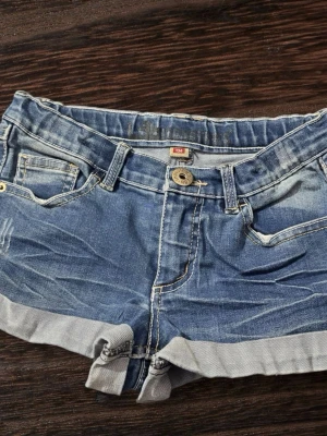 Blå jeansshorts från Lab Industries - Vi kan diskutera priset. Säljer ett par klassiska blå jeansshorts från Lab Industries. De har upprullade benslut, fem fickor och normal passform. Shortsen har knapp och dragkedja framtill samt bälteshällor. Perfekta för varma dagar och enkel att matcha med olika toppar. 