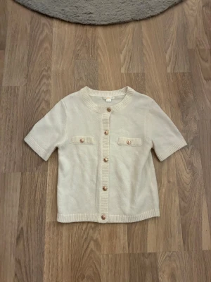 Kortärmad kofta - Super gullig vit kortärmad kofta från Gina Young med guld knappar på två fickor 