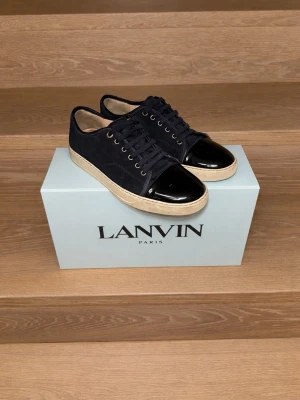 Svarta sneakers från Lanvin med lacktå - Snygga svarta sneakers från Lanvin med ovandel i mocka och kontrasterande svart lackad tå. Köpta på Care of Carl. Två dustbags, skosnören, box, allting ingår. Storleken är 41 men stora för sin storlek. Rekommenderar om man har 42-43.