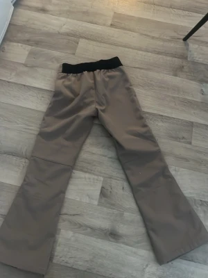 Beiga täckbyxor från 157 Funk strl 150 - Säljer ett par  beiga täckbyxor från 157 Funk i storlek 150. Byxorna har svart resår i midjan, dragkedja och knappar framtill samt quiltade detaljer över knäna. Perfekta för kalla dagar och vinteraktiviteter.