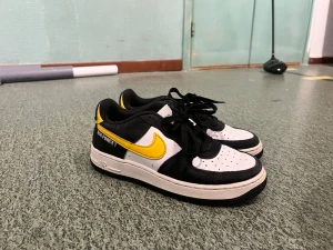 Nike Air Force 1 Athletic Club svart/gul - Säljer ett par Nike Air Force 1 Athletic Club sneakers i svart, vitt och gult. Skorna har klassisk låg siluett, svart mocka och vitt läder med gula detaljer och swoosh. Märkt 'Athletic Club' på hälen och perforerad tå för extra stil.