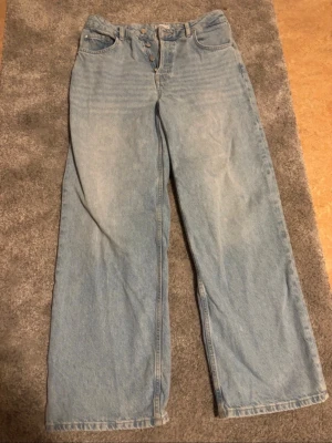 Ljusblå wide jeans S/M - Ljusblå jeans med raka, vida ben och hög midja. Klassisk femficksmodell med knäppning fram. Jeansen är tillverkade i denim och har en avslappnad passform. Perfekta för en chill och trendig look. Storlek W27 L32, S/M