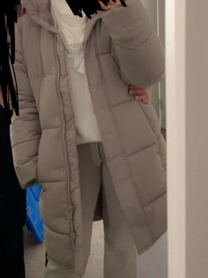 Beige lång pufferjacka med huva - Säljer en beige lång pufferjacka med huva och dragkedja framtill. Jackan har quiltad design och är perfekt för kalla dagar. Den har en avslappnad passform och långa ärmar, vilket gör den både snygg och bekväm. Från Hm i str xs, säljs för 550kr!