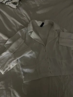 Vit satin blus med tajt midja  - Säljer en vit satin blus med tajtare midja som är V-ringad. Den har en dragkedja på sidan så den sitter åt kroppen finare. 