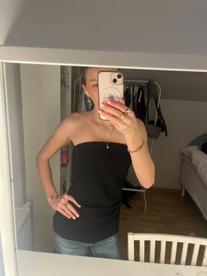 Svart tubtopp i enkel design - Säljer en svart, axelbandslös tubtopp med rak skärning och stilren look. Toppen är figurnära och har en klassisk bandeau-stil som passar perfekt till jeans eller kjol. Inte andvänd dock ingel prislapp kvar. Passar storlek S och XS. Sitter lite stor på mig även om jag vanligtvis har XS.
