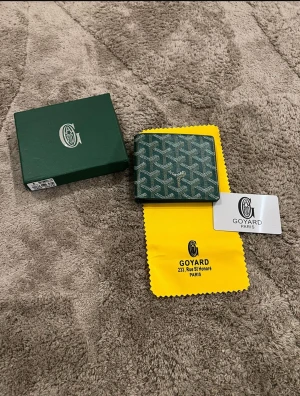 Grön mönstrad plånbok  - Säljer en grön plånbok med deras ikoniska grafiska mönster. Plånboken har flera kortfack och är tillverkad i skinn med vit och grå detaljering. Kommer med original ask, tygpåse och kort.