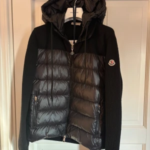 Svart cardigan från Moncler - Säljer en svart Moncler dunjacka med stickade ärmar och sidor samt quiltad front och huva. Jackan har dragkedja framtill, två fickor med dragkedja och Moncler-logga på ärmen. Perfekt för vår och höstdagar och riktigt snygg! Dammodell, fick den i julklapp och VÄLDIGT sparsamt använd, luvan är avtagbar, lite detaljer på smörerna jag kan skicka om man vill! ÄKTA såklart 🤗 Nypris på denhär gossen ligger på       11 000kr