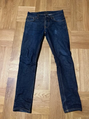 Nudie Jeans - Nudie jeans i modellen Grim tim Navy blue. I storlek 30/32. Väldigt starkt tyg därav är jeansen fortfarande i väldigt bra skick, bortsett från slitagen som visas på bilderna, pga accessoarer som har expanderat tyget.