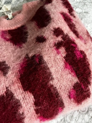 Rosa leopardmönstrad stickad tröja Garcia - Säljer en oanvänd fluffig stickad tröja från Garcia i rosa med vinröda och mörkrosa leopardfläckar. Tröjan har rund hals, ribbade muddar och en loose fit. Inköpt för 899 kr. 