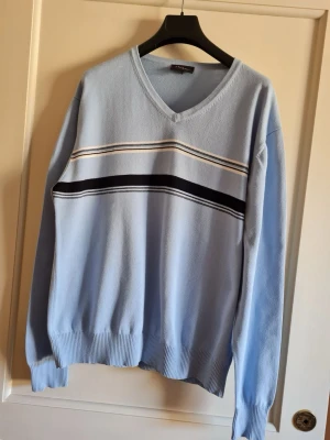 Ljusblå tröja från Atlant strl L - Säljer en ljusblå tröja från Atlant med v-ringning och ett stilrent randigt mönster i svart och vitt över bröstet. Tröjan har långa ärmar och ribbade muddar vid ärmslut och nederkant. 100% bomull. Storlek L (känns liten i storlek). Kan hämtas i Vallentuna.