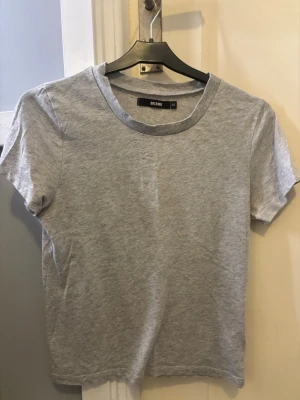 Grå basic t-shirt från BikBok  - Enkel och stilren grå t-shirt från BikBok i storlek XS. T-shirten har rund halsringning och korta ärmar, perfekt till jeans eller shorts. Tillverkad i mjuk bomull för en skön känsla hela dagen.