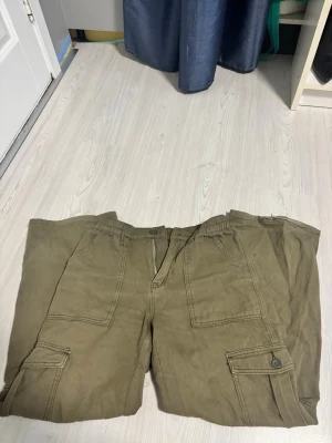 Khakigröna cargobyxor SHEIN - Khakigröna cargobyxor från SHEIN med stora fickor på sidorna och bak, elastisk midja och dragkedja fram. Byxorna har en loose passform. Perfekta för en avslappnad streetstil.