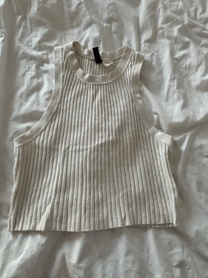 Ribbad beige linnetopp - Säljer en ribbad beige linnetopp med hög halsringning och ärmlös design. Toppen har en croppad passform och är tillverkad i ett mjukt, stretchigt material som känns skönt mot huden. Perfekt för varma dagar eller som layering-plagg.