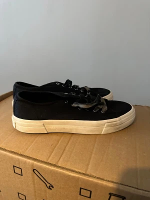 Svarta sneakers från Vagabond - Säljer ett par klassiska svarta sneakers från Vagabond med vit, tjock sula och svarta snören. Skorna har rund tå och metallöljetter. Ovandelen är i tyg och sulan i gummi, perfekt för en clean och enkel stil.
