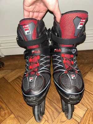 Fila X-One svarta och röda inlines - Säljer ett par Fila X-One inlines i svart och rött med cool design. Skorna har snörning, kardborreband och spänne för extra stöd. Ovandelen är i mesh och syntetmaterial för bra ventilation. Fyra hjul per sko och robust ram för stabilitet. Justerbar storlek 38-41