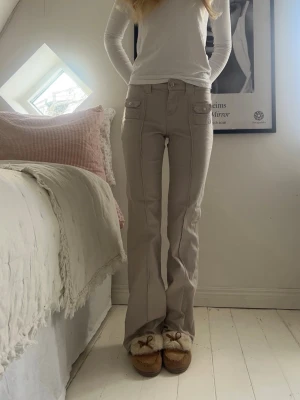 Byxor  - Såå snygga beiga byxor/jeans med supercoola detaljer! Innerbenslängd: 82cm, midjemått rakt över: 35cm