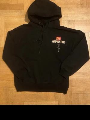 Svart Cactus Jack x McDonald's hoodie M - Svart hoodie från Cactus Jack x McDonald's med tryck 'APPLE PIE' och McDonald's-logga fram, samt 'ALWAYS HAD A THING FOR SWEETS' och Cactus Jack-tryck bak. Stor känguruficka, snörning i huvan och mjukt material i bomull och polyester. Perfekt för dig som gillar limited edition streetwear.