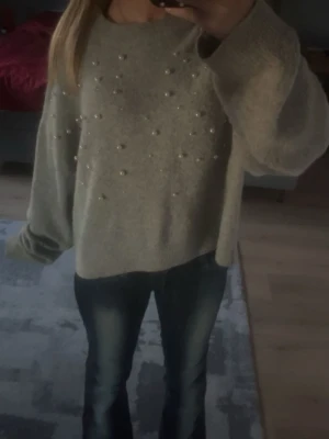 Grå stickad tröja med pärlor - Säljer en oversized grå stickad tröja med dekorativa pärlor framtill. Tröjan har rund halsringning, långa ärmar och en mjuk, mysig känsla. Perfekt för dig som gillar en avslappnad men ändå trendig stil.