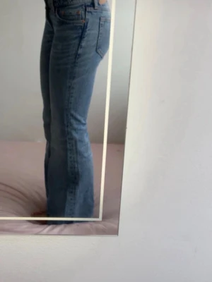Blå bootcut jeans med hög midja - Snygga blå bootcut jeans med hög midja och klassisk femficksdesign. Jeansen har en lätt tvättad look och raka ben som går ut lite nedtill. Perfekta till en trendig vardagsstil och passar till crop tops eller hoodies.