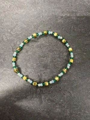 Grönt och guldigt pärlarmband storlek XL - Säljer ett armband med pärlor i grönt, ljusblått och guld. 