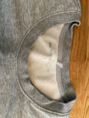 Grå sweatshirt från Emporio Armani - Stilren grå sweatshirt från Emporio Armani med svart logotyptryck på bröstet. Tröjan har rund halsringning, långa ärmar och ribbade muddar vid ärmslut och nederkant. Perfekt för en avslappnad och trendig look.