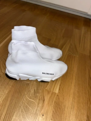 Vita Speed Trainer sneakers - Säljer ett par vita Speed Trainer sneakers med stickad ovandel och chunky sula. Skorna har en strumpliknande passform och -logga på sidan. Sulan är svart och vit med tydlig struktur undertill. Riktigt clean och modern look.