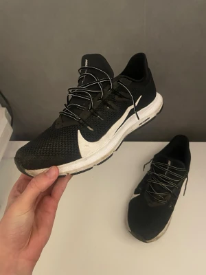Nike svartvita löparskor - Snygga svartvita Nike sneakers med ventilerande mesh-överdel och vit sula. Skorna har en stor vit swoosh på sidan och svarta snören. Perfekta för dig som gillar sportig stil och vill ha bekväma skor till vardags. Låg modell som ger en clean look.