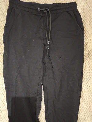 Svarta mjukisbyxor från KappAhl - Svarta mjukisbyxor från KappAhl med dragsko i midjan och sidofickor. Tillverkade i mjukt och bekvämt material, perfekta för chill dagar. Klassisk rak passform och enkel design som funkar till det mesta.