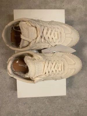 Maison Margiela sneakers  - Unika vita sneakers från Maison Margiela med råa kanter och grovsydd sula. Skorna har klassisk snörning och en cool, avslappnad vibe. Perfekta för dig som gillar statement-plagg och vill sticka ut med en trendig och kreativ look. Storleken är 38 men sitter som 39/39,5. Pris kan diskuteras