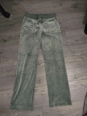 Gröna Juicy Couture - Mysiga gröna mjukisbyxor från Juicy Couture i mjuk velour. Byxorna har bred resårmidja med dragsko, stora fickor fram och diskret broderad logga på ena fickan. Perfekta för chill dagar eller när du vill vara extra bekväm.