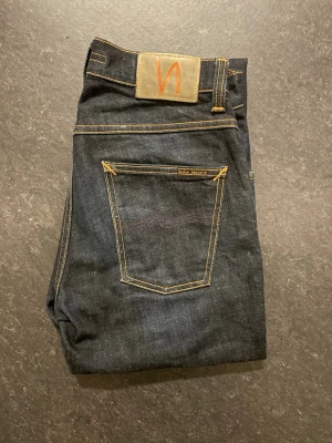 Nudie jeans Grim Tim - Säljer ett par mörkblåa Nudie jeans Grim Tim Dry True Navy, storlek W29/L32, slim fit. Mycket fint skick där de använts fåtal gånger. Jeans har fått en snygg påbörjad tvätt på knänaoch har inte tvättas nån gång. Tyvärr har de en fåtal defekter (se bild)                                                             Nypris 1600kr                                                   Mått: A=38cm B=80cm C=108cm D=16cm  Fråga gärna om fler bilder eller om det är något ni generellt undrar!                 