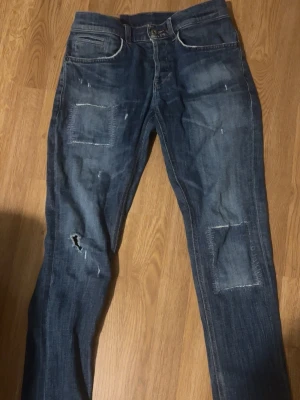 Dondup jeans  - Säljer ett par mörkblå Dondup  jeans med raka ben och coola patchade detaljer på båda benen. Jeansen har slitningar och lagade partier framtill som ger en trendig och avslappnad look. Klassisk femficksmodell och normal midja.