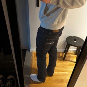 Mörkblå jeans från Nudie Jeans, rak modell - Säljer ett par mörkblå jeans från Nudie Jeans med klassisk rak passform som passar alla och kontrastsömmar. Jeansen har en tydlig och snygg logga på bakfickan och läderpatch i midjan. Är nästan helt oanvända. Hör av er vid intresse🤗