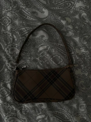 Brun rutmönstrad axelväska - Snygg brun handväska med rutigt mönster och kort axelrem. 