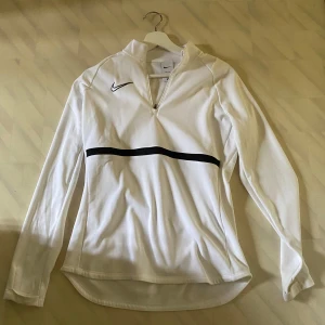 Nike vit träningströja - Säljer en vit långärmad träningströja från Nike Tröjan är tillverkad i Dri-FIT-material som andas och passar perfekt till träning. Har använt den en gång storlek S 