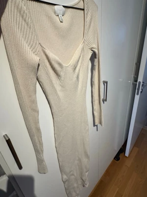Beige ribbad långklänning H&M - Säljer en beige ribbad långklänning från H&M med v-ringning och långa ärmar. Klänningen har en figurnära passform och är tillverkad i mjukt, stretchigt material som sitter snyggt på kroppen. Använd endast 2-3 gånger!!