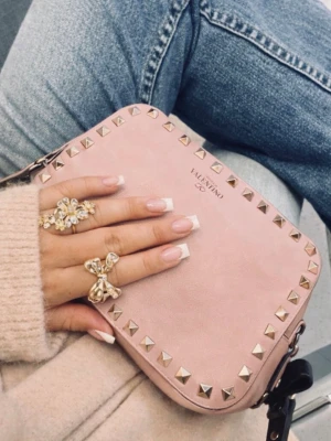 Rosa axelväska från Valentino rockstud garavani - Säljer en snygg rosa axelväska från Valentino med guldiga nitar runt kanterna. Väskan har en stilren, rektangulär form och justerbar axelrem. Perfekt för dig som vill ha en trendig accessoar med lyxig känsla.