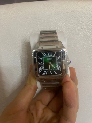 Seiko fyrkantig klocka i silver - Stilren Seiko klocka med fyrkantig boett i silverfärgat stål och länkarmband. Urtavlan är grön med svarta och vita detaljer samt romerska siffror. Automatisk rörelse synlig på baksidan. Perfekt accessoar för en modern look. Helt ny och en fin låda medföljer 