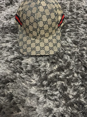Gucci keps med GG-mönster - Snygg keps från Gucci i beige canvas med klassiskt GG-monogram över hela kepsen. Röd och grön rand på sidorna och justerbar rem baktill i svart läder med präglad Gucci-logga. Perfekt accessoar för en trendig streetstyle-look. BYTER GÄRNA MED NÅGOT PRIS KAN SÄNKAS 