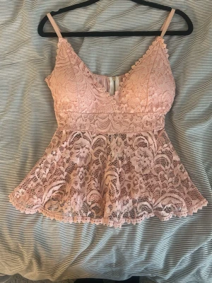 Rosa spetslinne med volang - Supersött rosa linne med tunna axelband och v-ringning. Toppen har ett peplum-aktigt fall och är helt täckt av blommig spets. Dragkedja bak för enkel påklädning. Perfekt för dig som gillar romantisk och feminin stil. stretchig PRIS KAN DISKUTERAS 