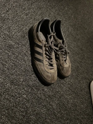 Adidas Spezial grå sneakers mocka - Säljer ett par Adidas Spezial sneakers i grå mocka med svarta detaljer och klassiska tre ränder på sidan. Guldfärgad 'SPEZIAL' text på sidan och svart yttersula. Skön retrostil och tidlös design som passar till det mesta.