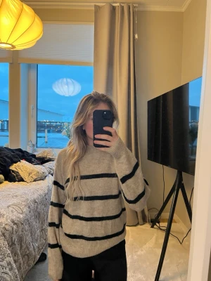 Beige stickad tröja med svarta ränder - Stickad tröja från H&M i beige med breda svarta horisontella ränder. Tröjan har en avslappnad passform, rund halsringning och ribbade muddar vid ärmslut och nederkant. Perfekt för lager-på-lager och en chill look.